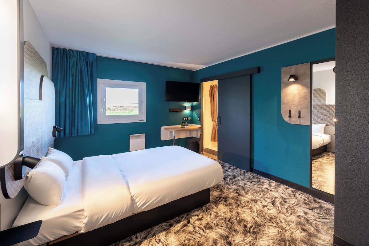 A modern hotel room with a large bed, a bathroom with a mirror, and a view of the outdoors.
