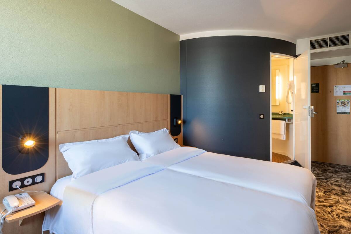 A hotel room with a large bed, bedside tables, a phone, and a door leading to a bathroom.