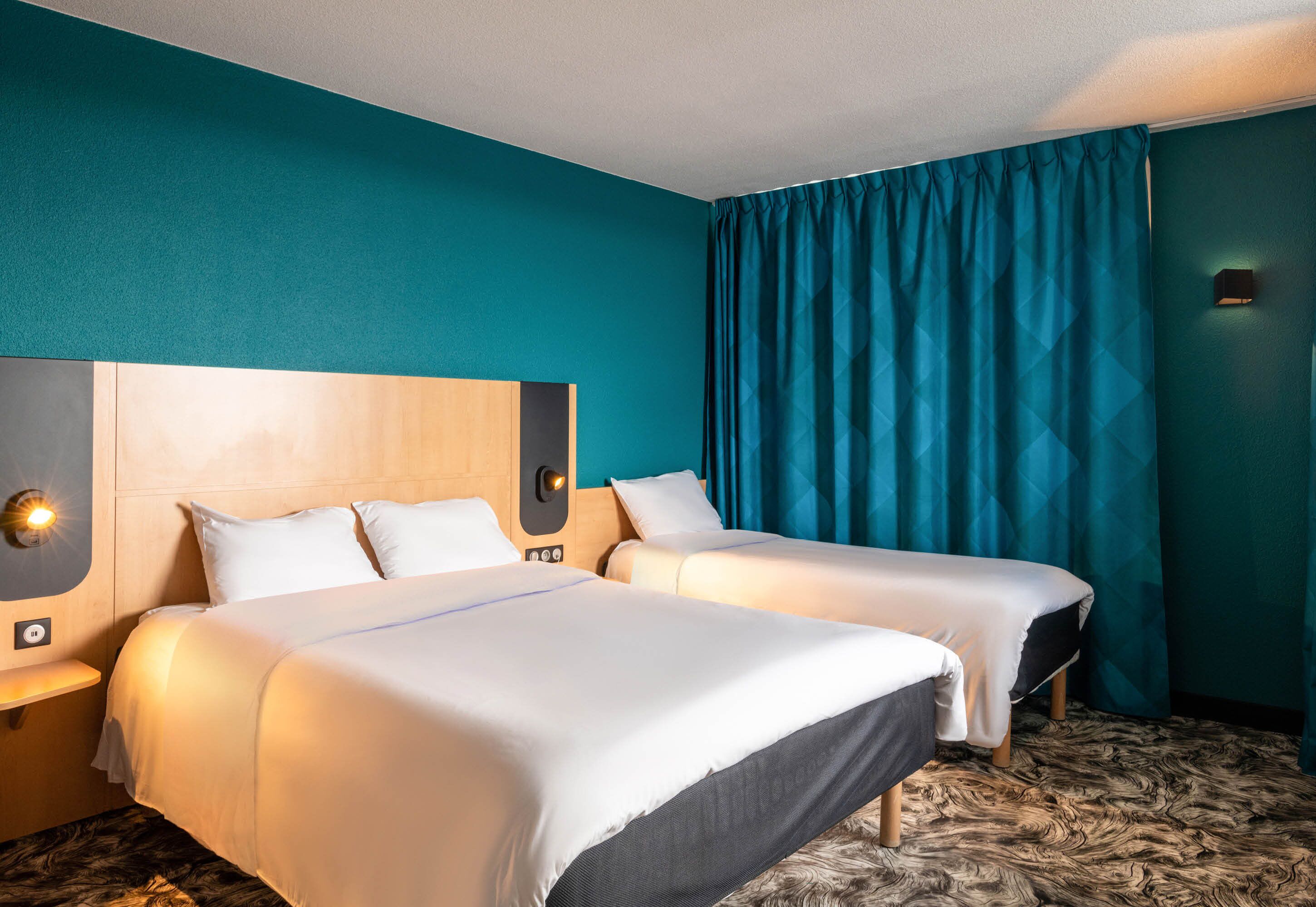 A hotel room with two beds, teal walls, and a patterned carpet.