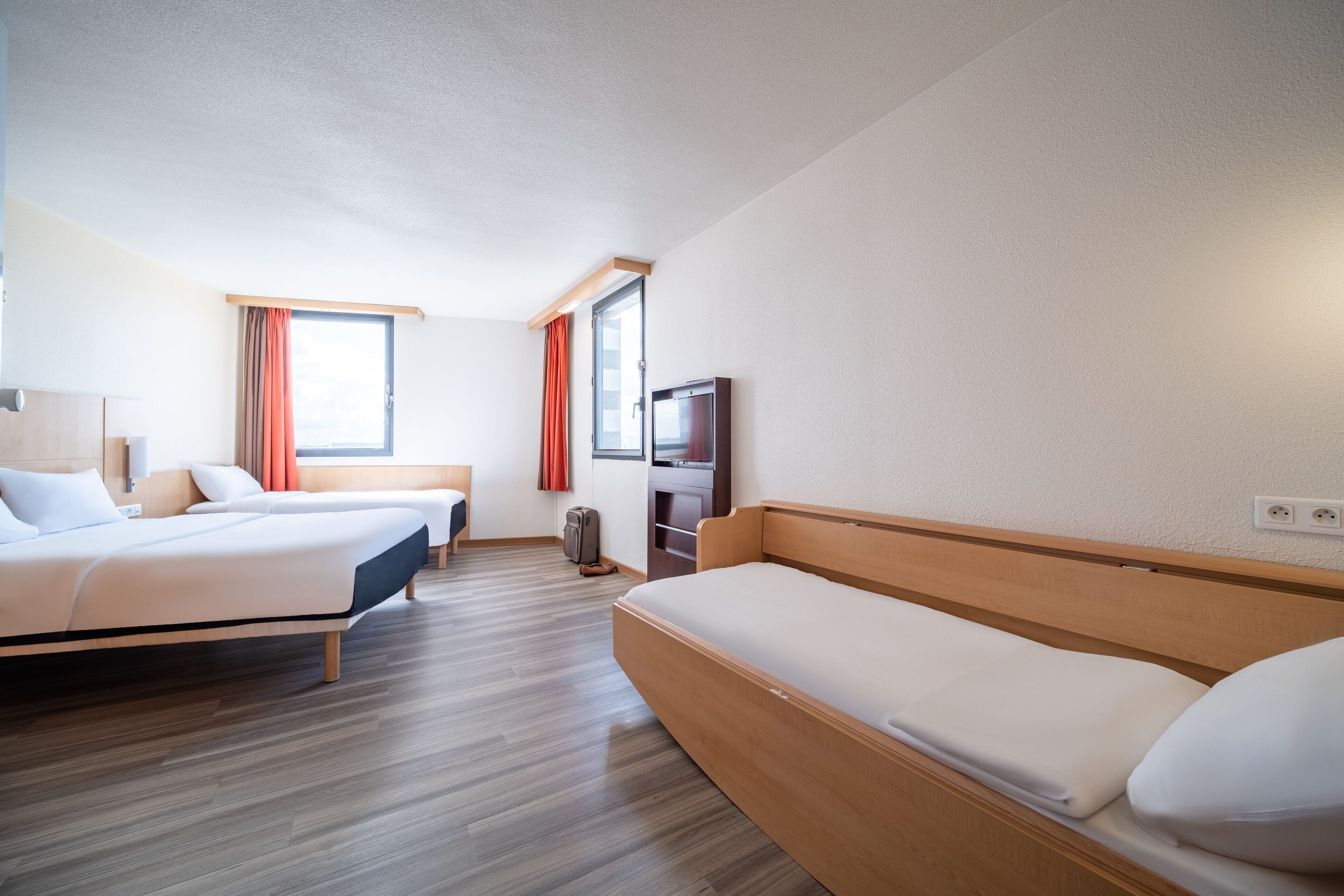 A hotel room with two beds, a TV, and a wooden bench.