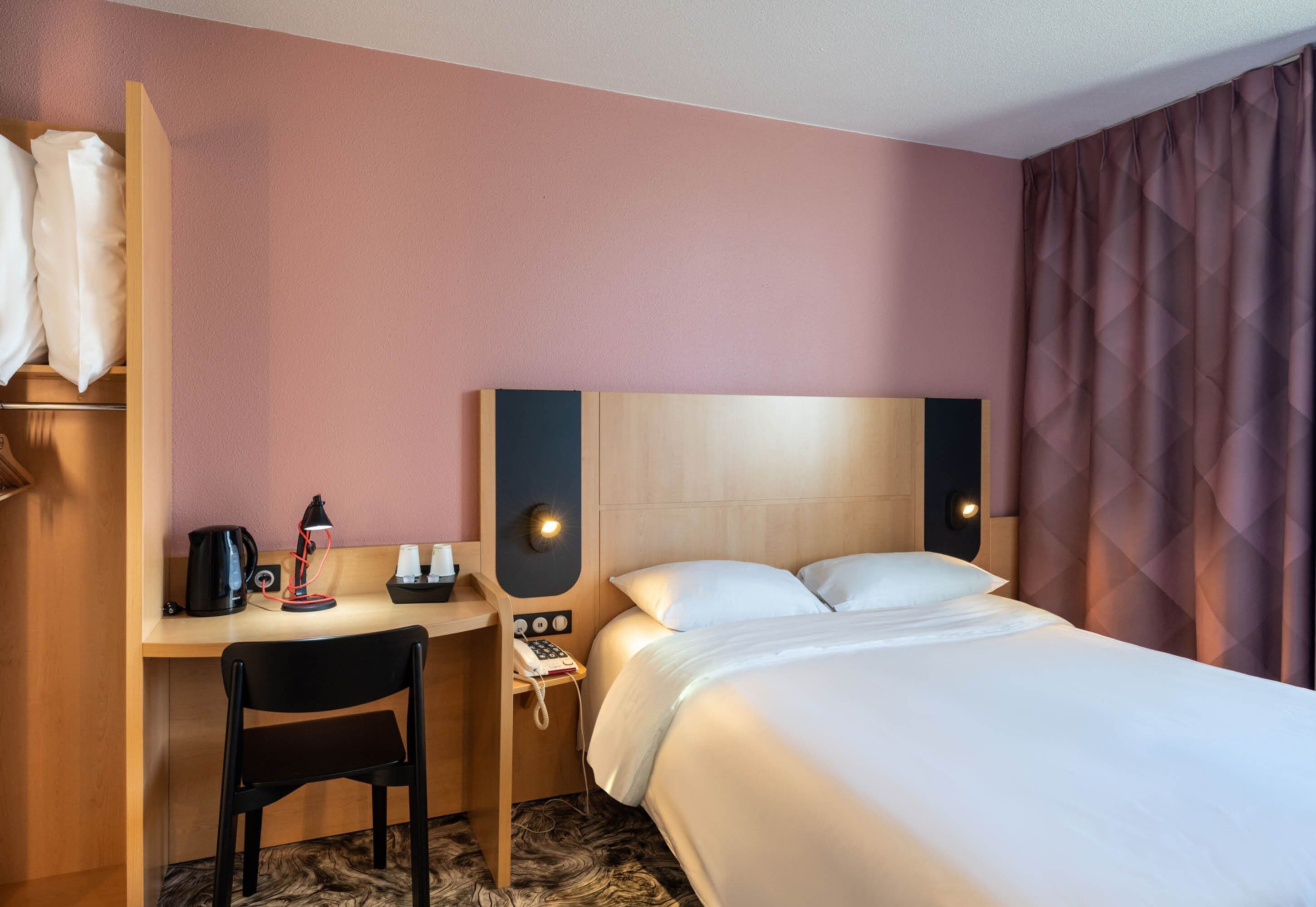 A hotel room with a bed, a desk with a chair, a telephone, and a coffee maker.