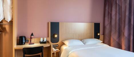 Una habitación de hotel con una cama, un escritorio con silla, un teléfono y una cafetera.