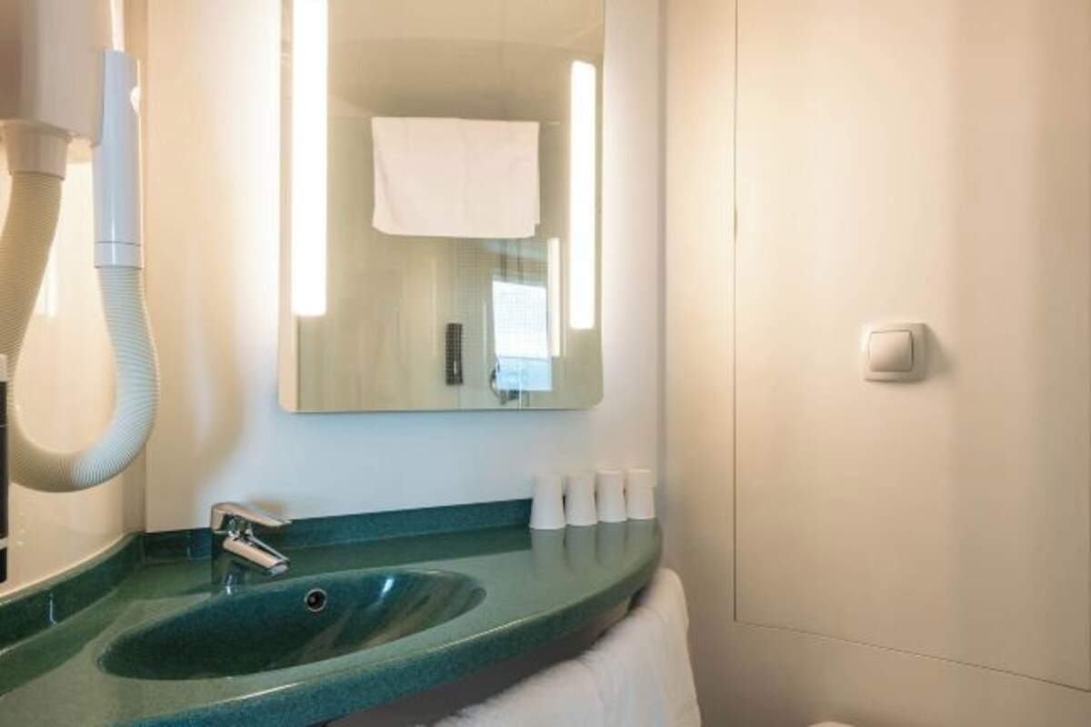 Un baño con un lavamanos verde, un espejo, una toalla colgada en la pared y un secamanos.
