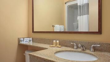 A bathroom with a granite countertop sink, two faucets, and a mirror above it. There are toiletries on the countertop and a shower curtain visible in the mirror reflection.