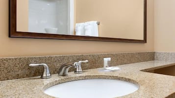 Un baño con encimera de granito, lavabo, dos llaves y un espejo.