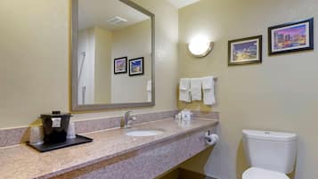 Un baño con encimera de granito, un lavabo, un inodoro y un espejo grande. Hay cuadros enmarcados en la pared y un perchero con toallas.