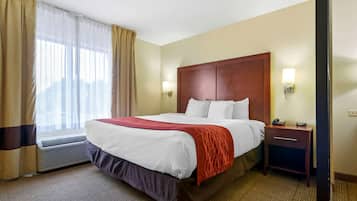 Habitación de hotel con una cama grande, una mesita de noche con lámpara y una ventana con cortinas.