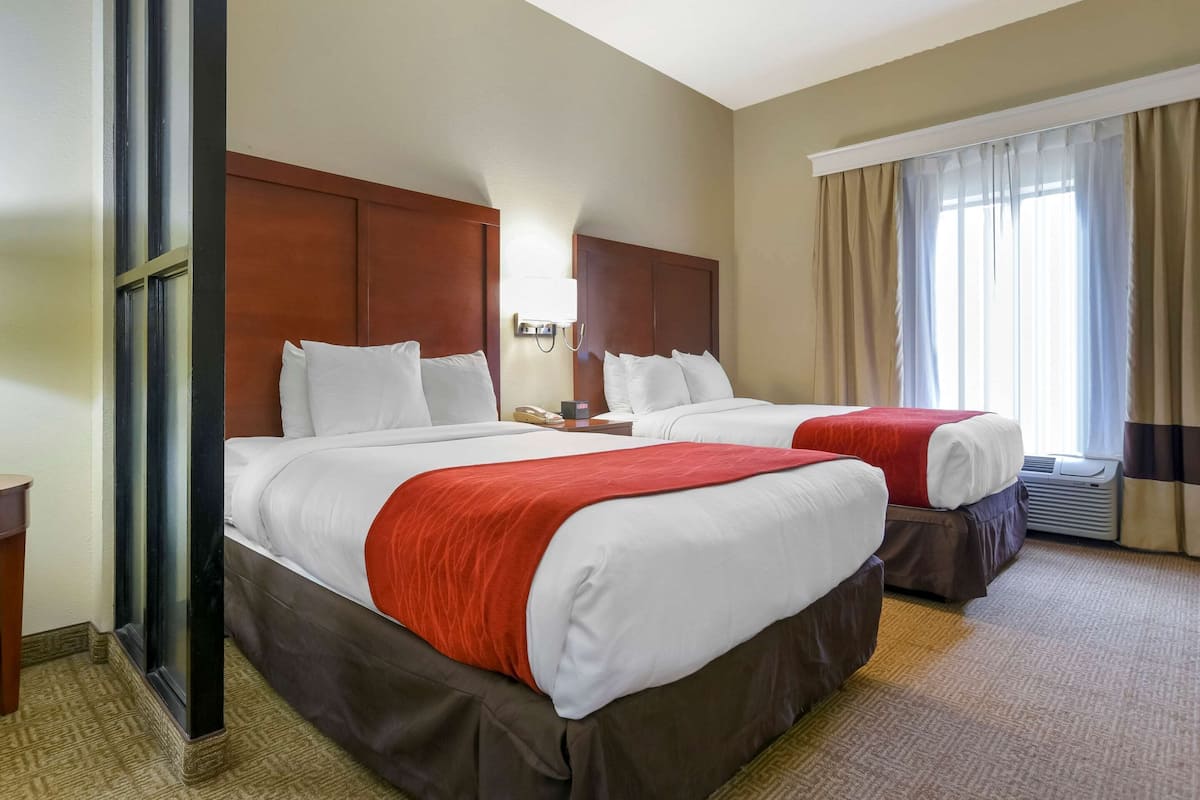 Une chambre d’hôtel avec deux lits, une tête de lit en bois, une table de chevet avec une lampe et une fenêtre avec des rideaux.