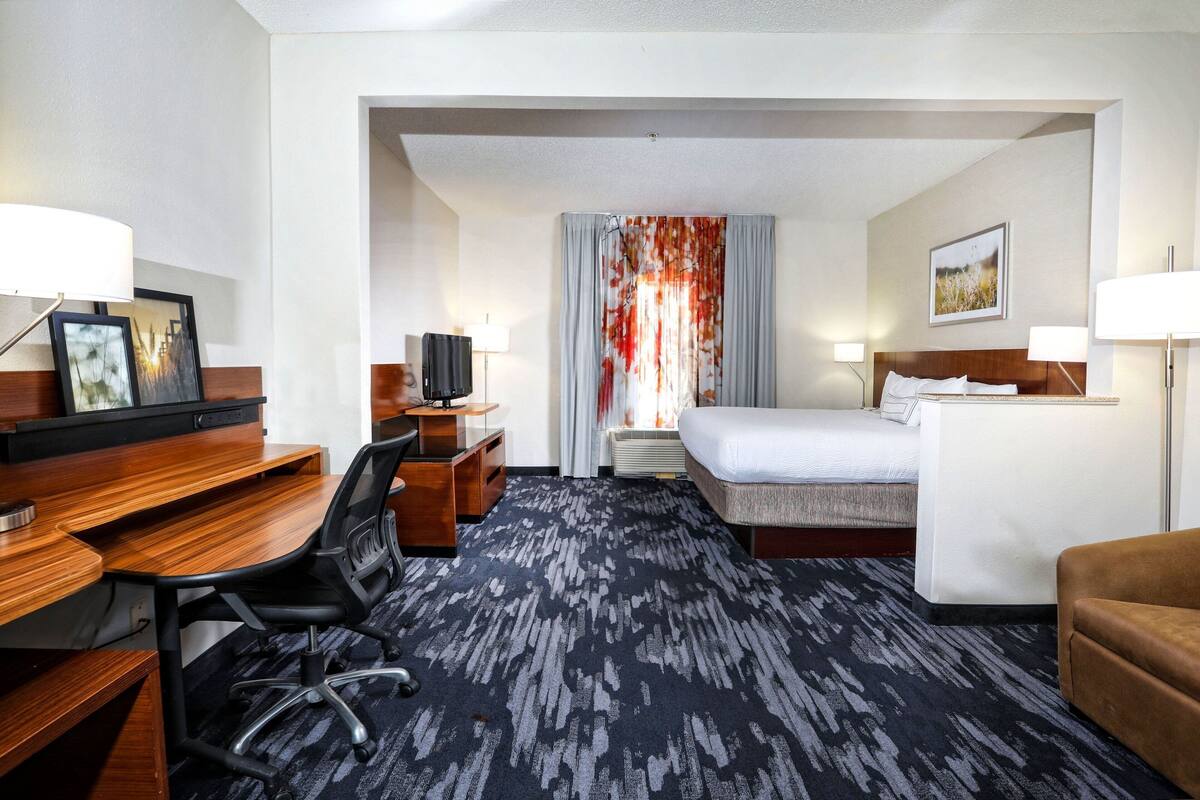 A hotel room with a bed, desk, chair, and a TV.