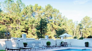Piscina con sillas de descanso y sombrillas, rodeada de árboles.