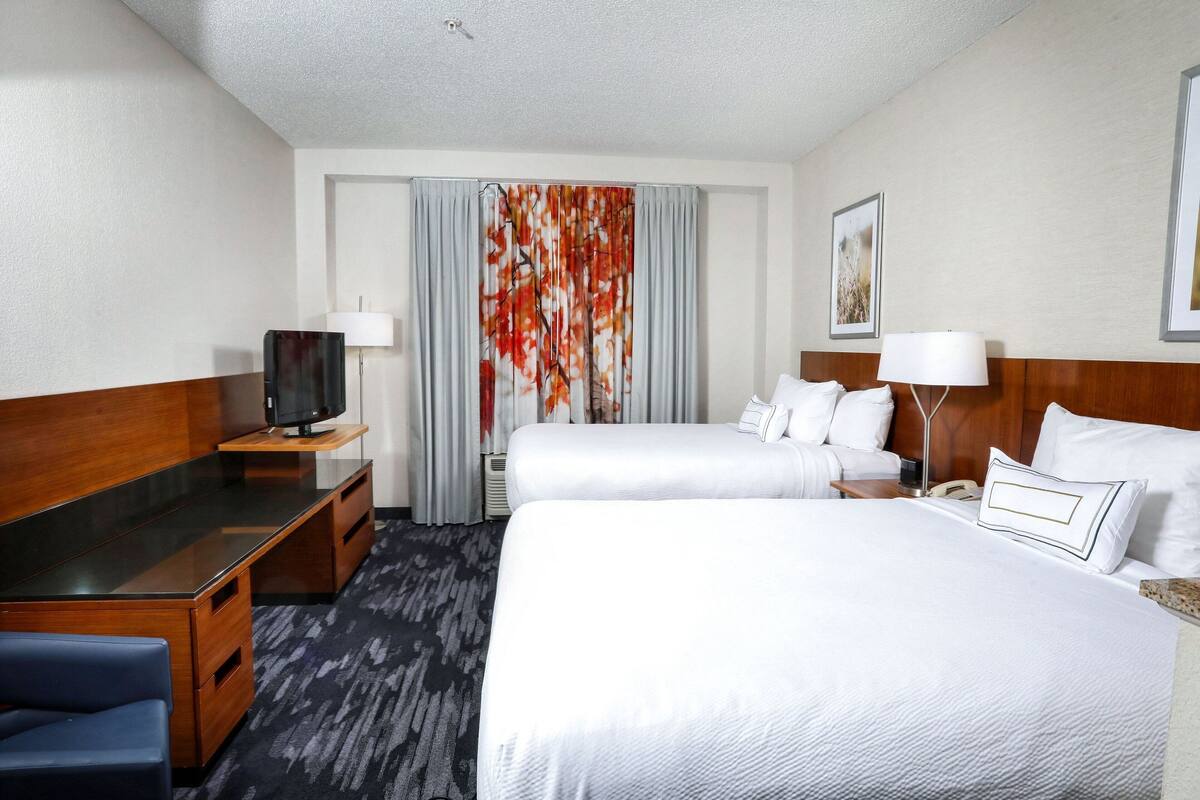 A hotel room with a desk, two beds, a TV, and a window with curtains.