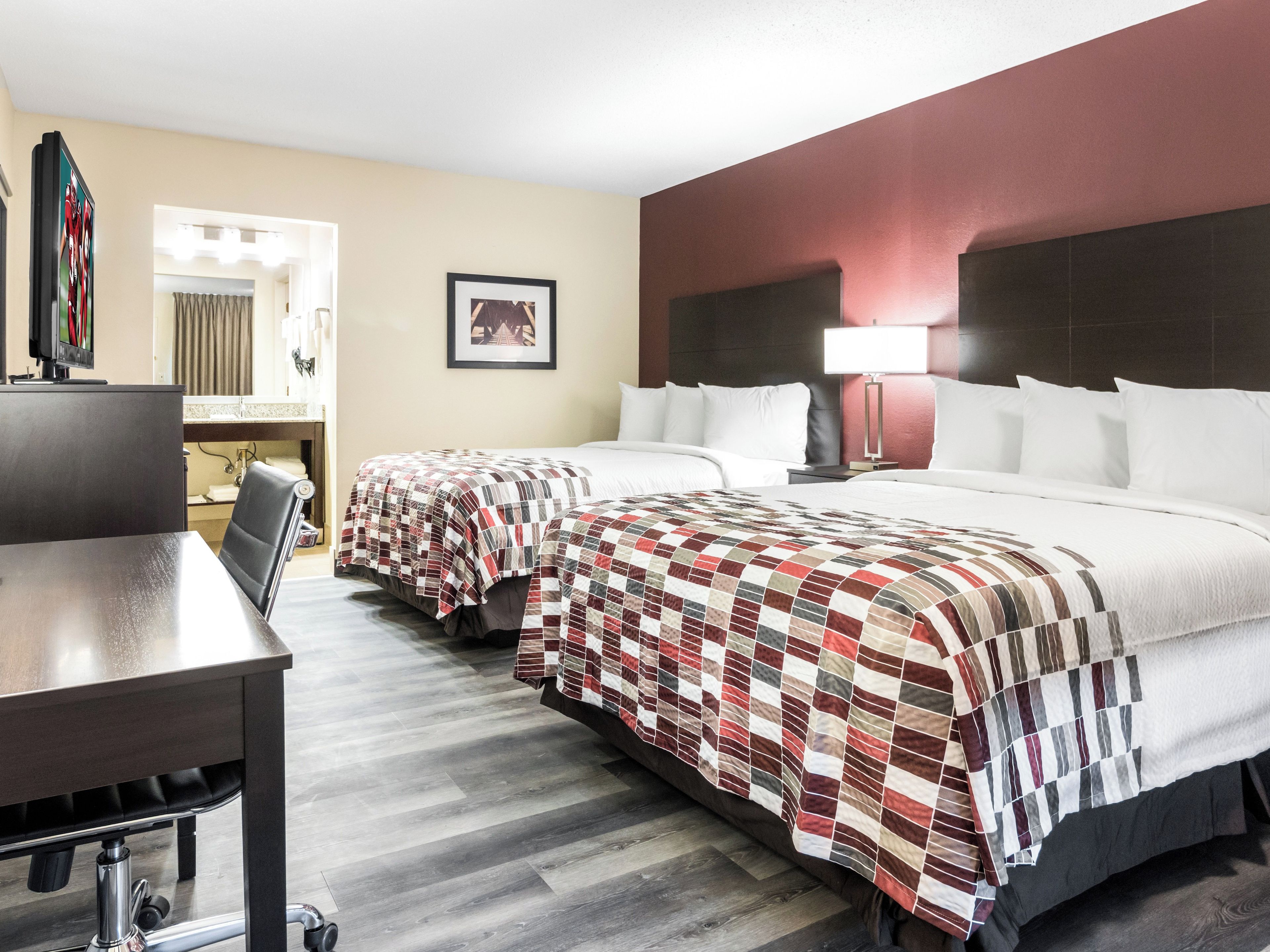 A hotel room with two beds, a desk, and a bathroom visible in the background.