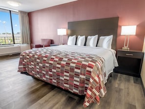 Una habitación de hotel con una cama grande, una mesita de noche con lámpara, una silla y una ventana con cortinas.