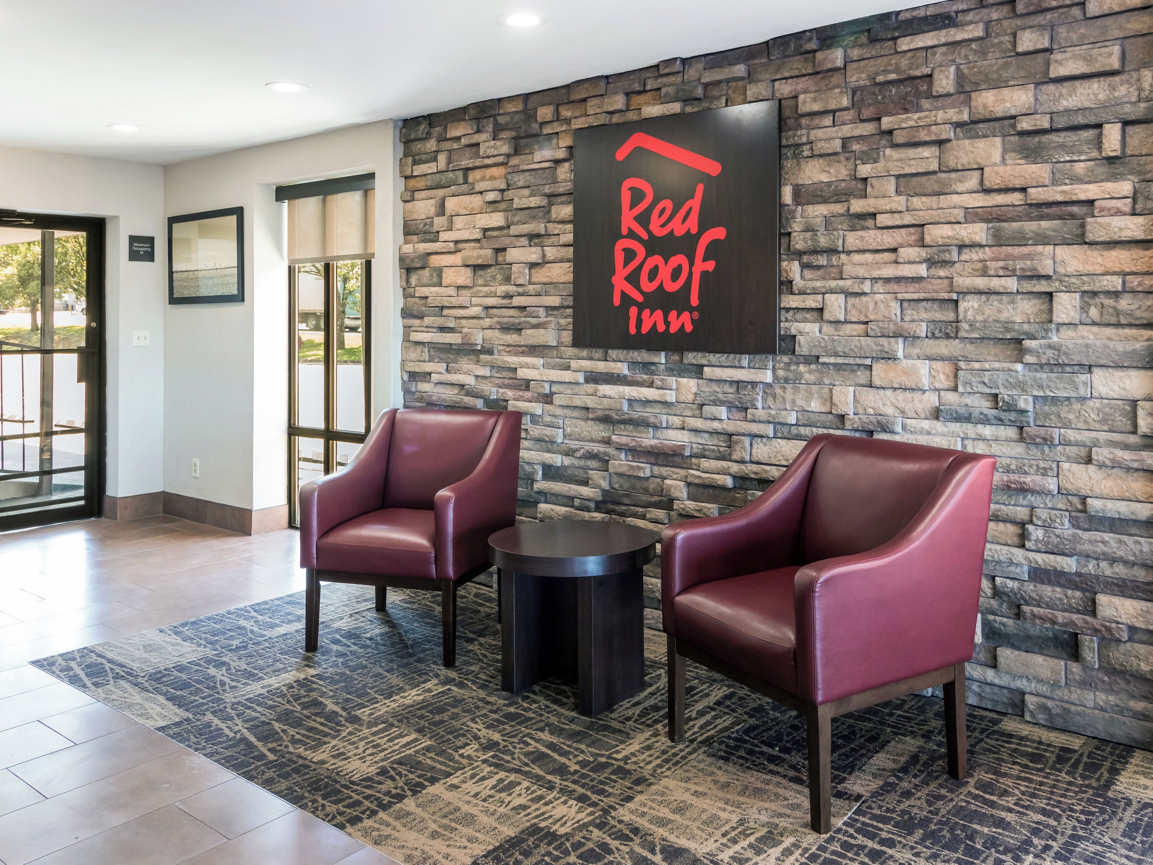 En lobby i ett Red Roof Inn-hotell med två läderfåtöljer, ett litet bord och en vägg av sten.