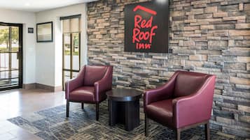 En lobby i ett Red Roof Inn-hotell med två läderfåtöljer, ett litet bord och en vägg av sten.
