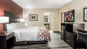 A hotel room with a bed, a desk, a television, and a bathroom visible in the background.