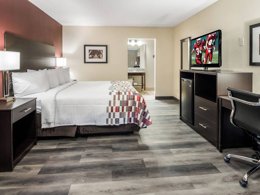 A hotel room with a bed, a desk, a television, and a bathroom visible in the background.