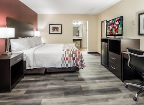 Habitación de hotel con una cama, un escritorio, un televisor y un baño visible al fondo.