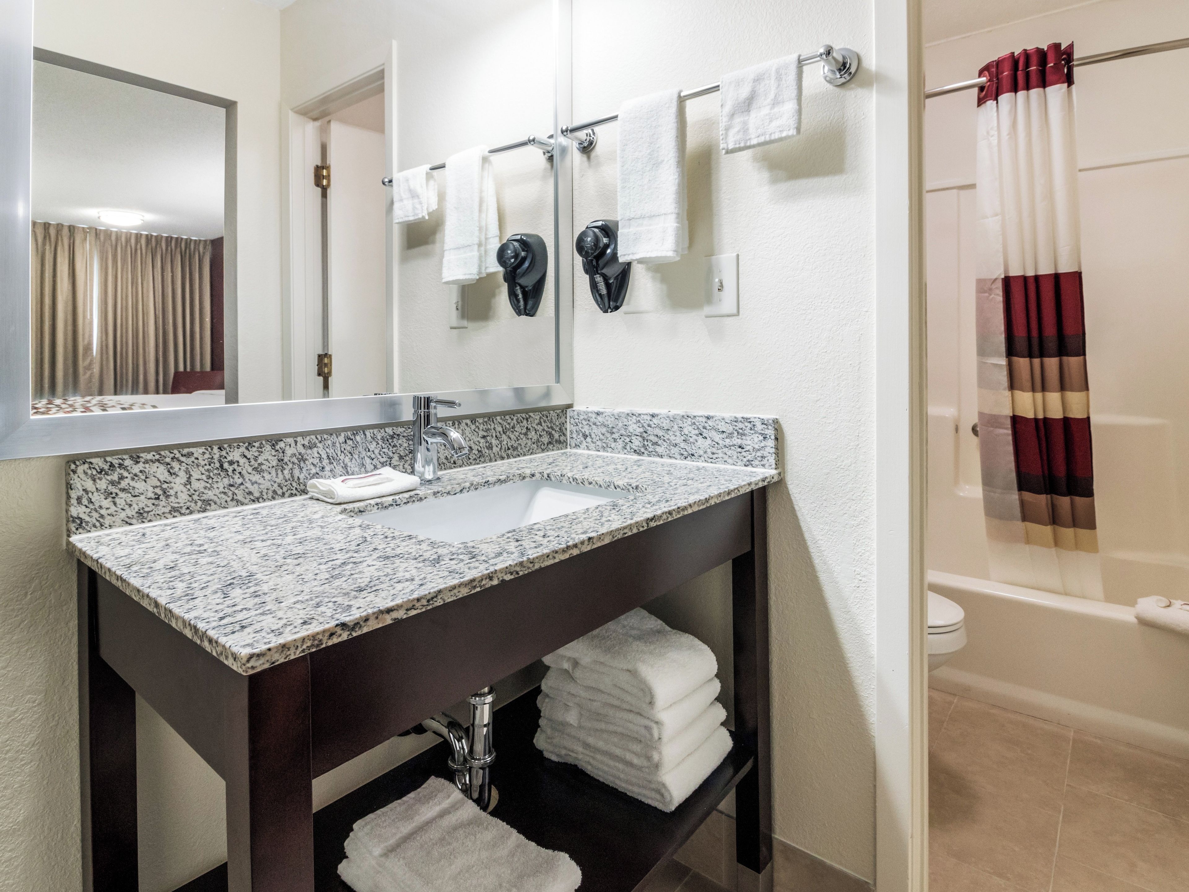 Un baño con lavamanos de encimera de granito, un espejo, un perchero con dos toallas y un cortinón de ducha.