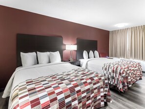 A hotel room with two beds, a nightstand, a lamp, and a window with curtains.