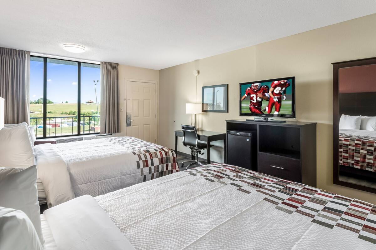 Une chambre d’hôtel avec deux lits, un bureau, une télévision et une grande fenêtre donnant sur l’extérieur.
