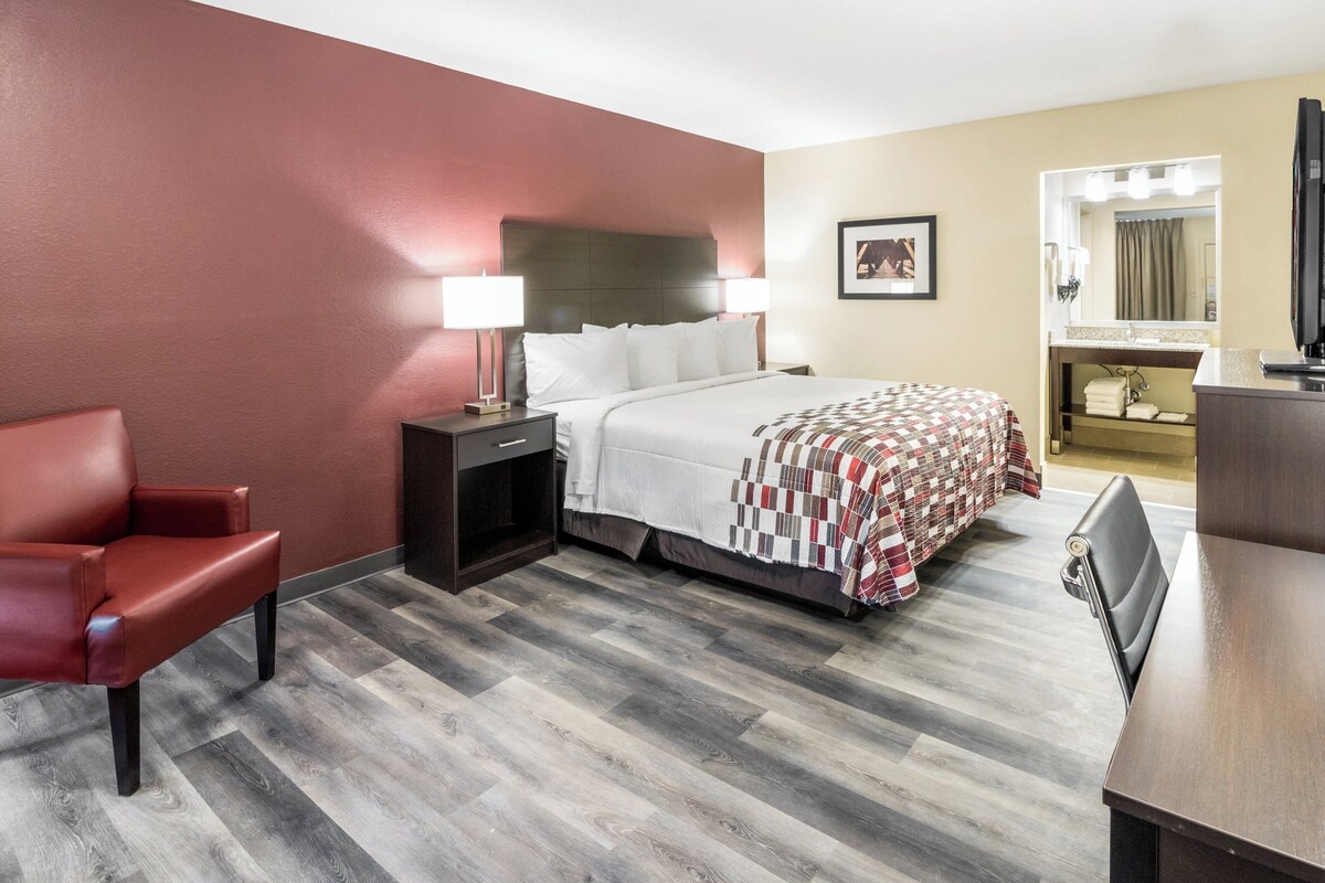 A hotel room with a bed, a desk, a chair, a nightstand, and a mirror.