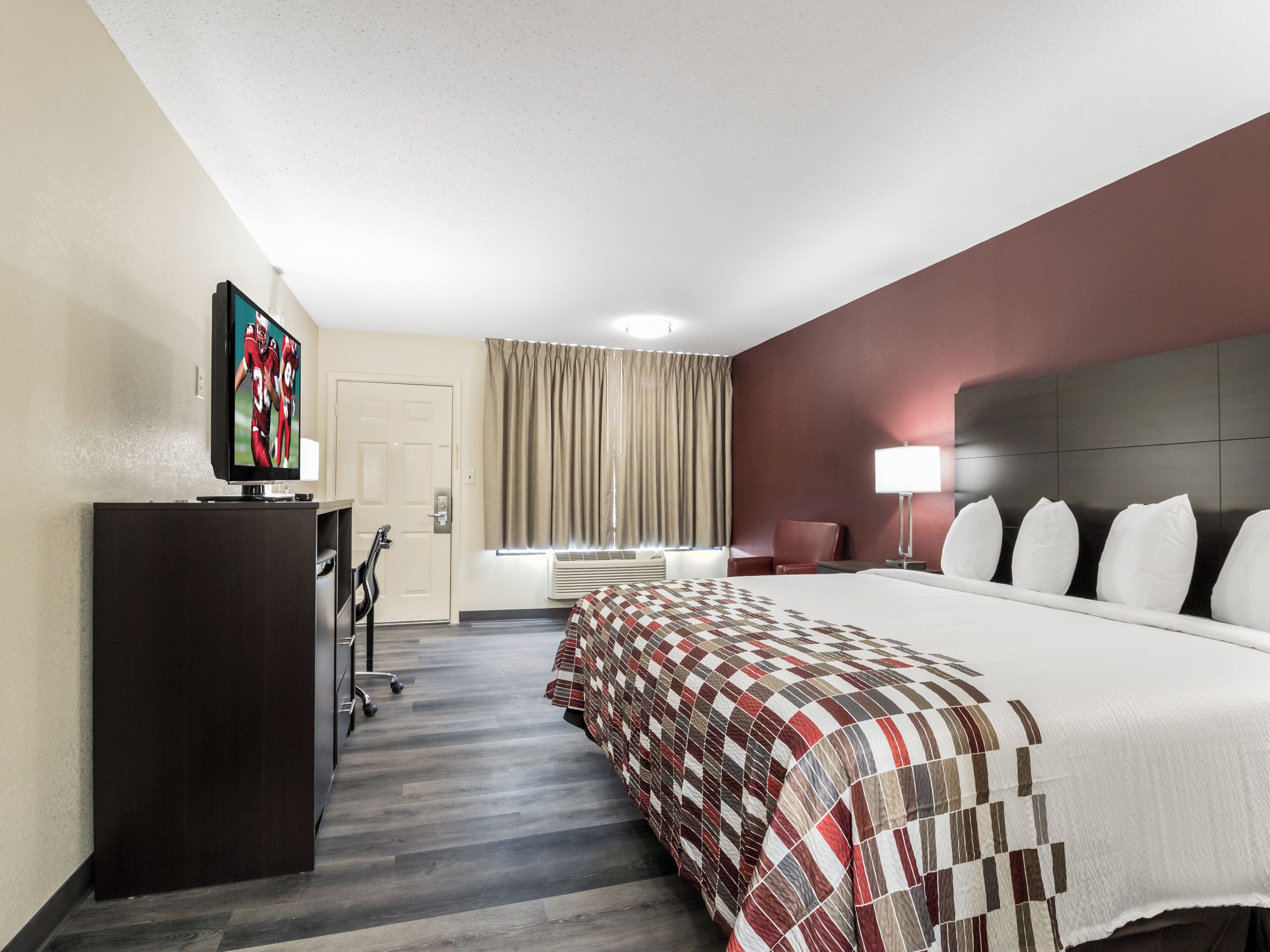 A hotel room with a bed, a desk, a television, a chair, and a lamp.