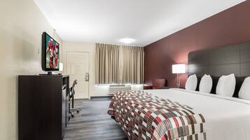 A hotel room with a bed, a desk, a television, a chair, and a lamp.