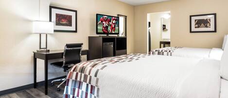 A hotel room with a bed, desk, chair, TV, and artwork on the walls.