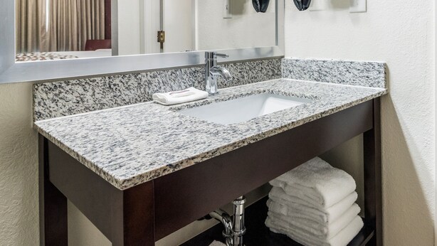 A bathroom with a granite countertop sink, a mirror, and a towel rack with multiple towels. - Red Roof Inn Dandridge (Dandridge)