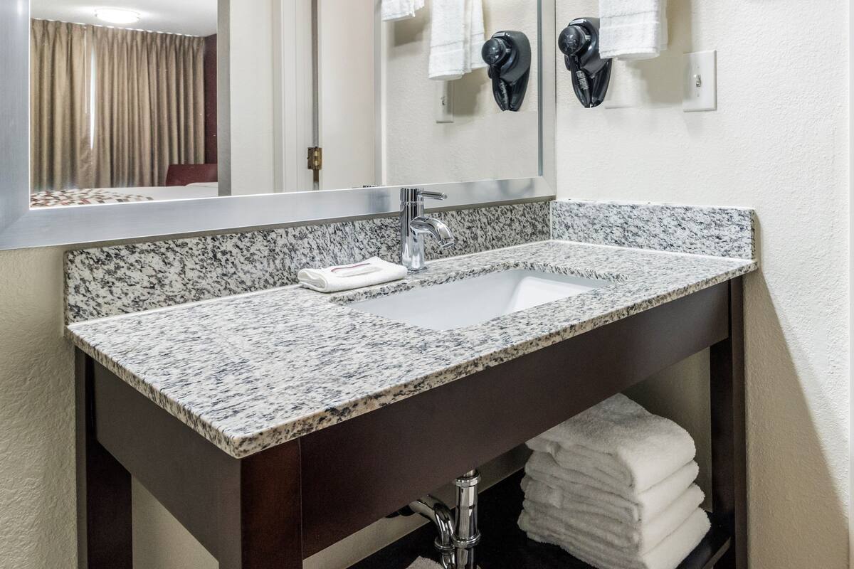 A bathroom with a granite countertop sink, a mirror, and a towel rack with multiple towels.