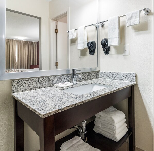 A bathroom with a granite countertop sink, a mirror, and a towel rack with multiple towels. - Red Roof Inn Dandridge (Dandridge)