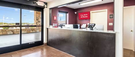 A hotel reception area with a check-in counter, a view of the parking lot, and a sign indicating free Wi-Fi availability.