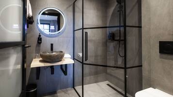 A modern bathroom with a glass-enclosed shower, a round mirror, a stone sink, and a toilet.