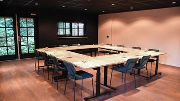 Un salón de conferencias con una larga mesa, sillas y una ventana con vistas a árboles.