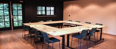 Un salón de conferencias con una larga mesa, sillas y una ventana con vistas a árboles.