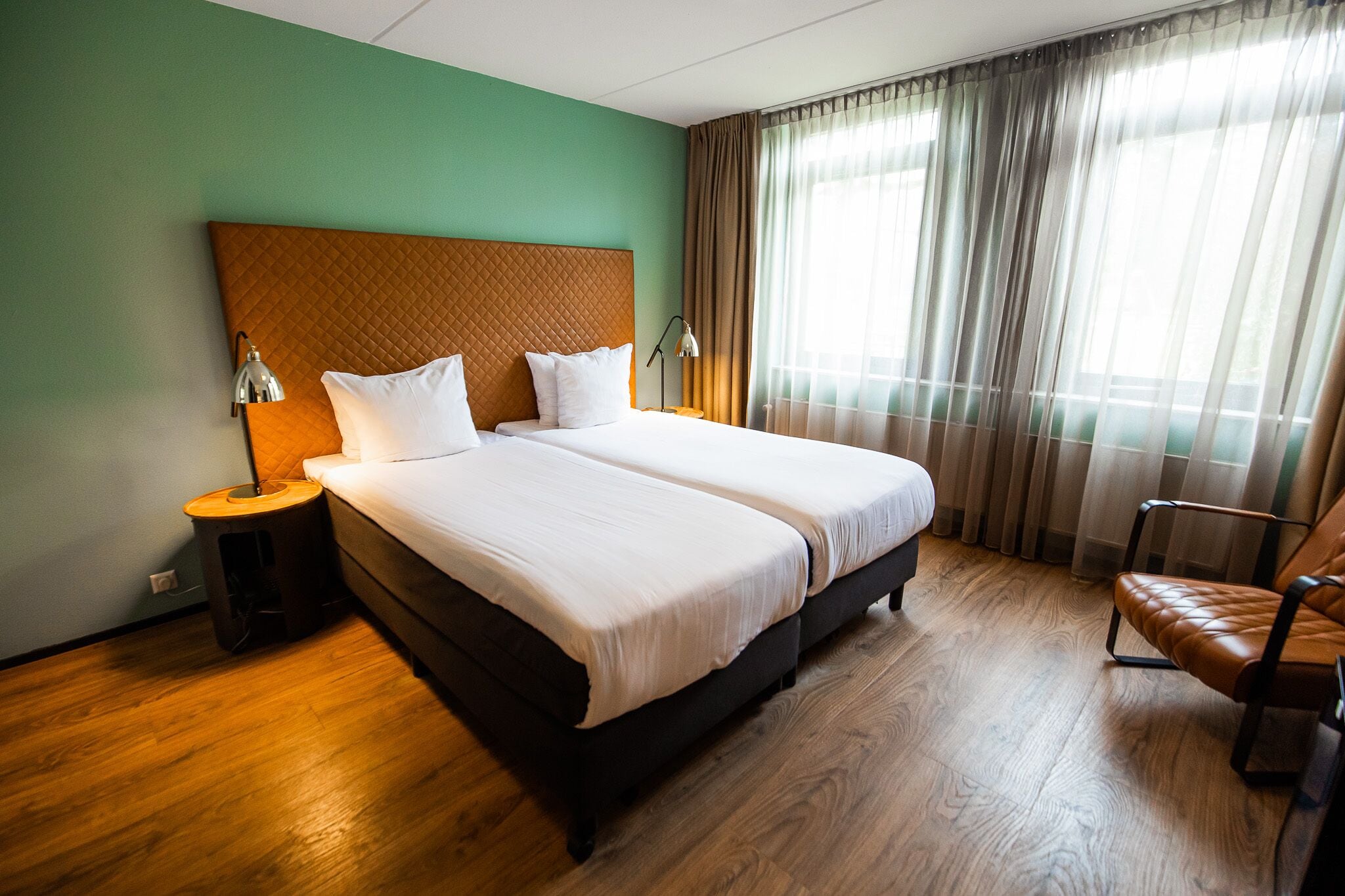 Una habitación de hotel con una cama grande, dos mesitas de noche, una silla y una ventana con cortinas.