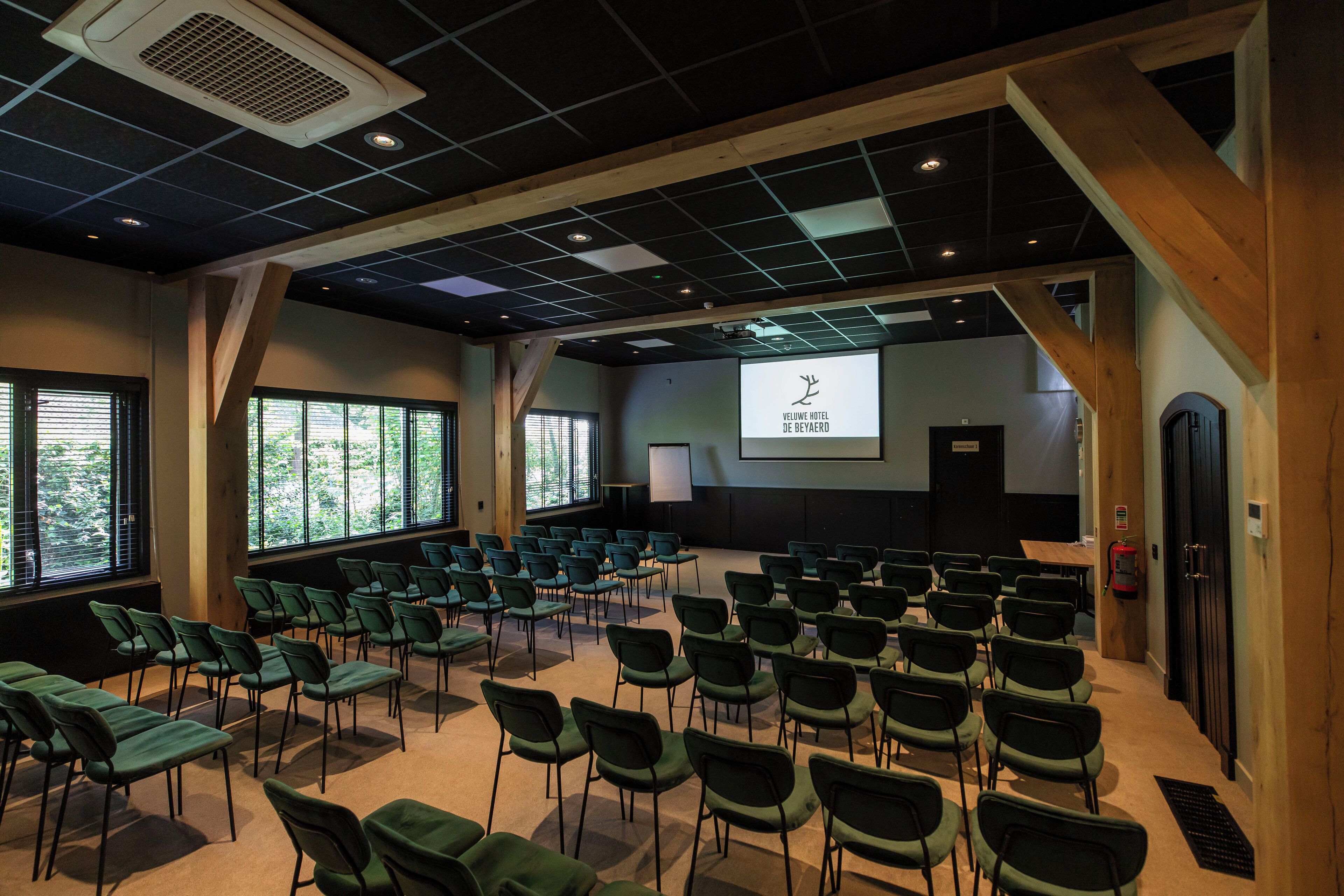 Una sala de conferencias con filas de sillas, una pantalla de proyector y un amplio ventanal.