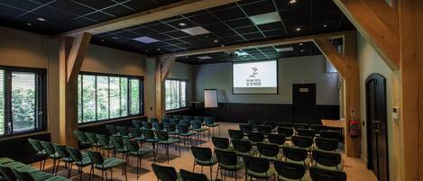 A conference room with rows of chairs, a projector screen, and a large window.
