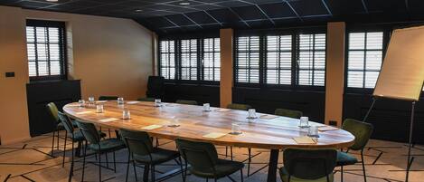 Un salón de conferencias con una mesa larga, sillas verdes y ventanas amplias.