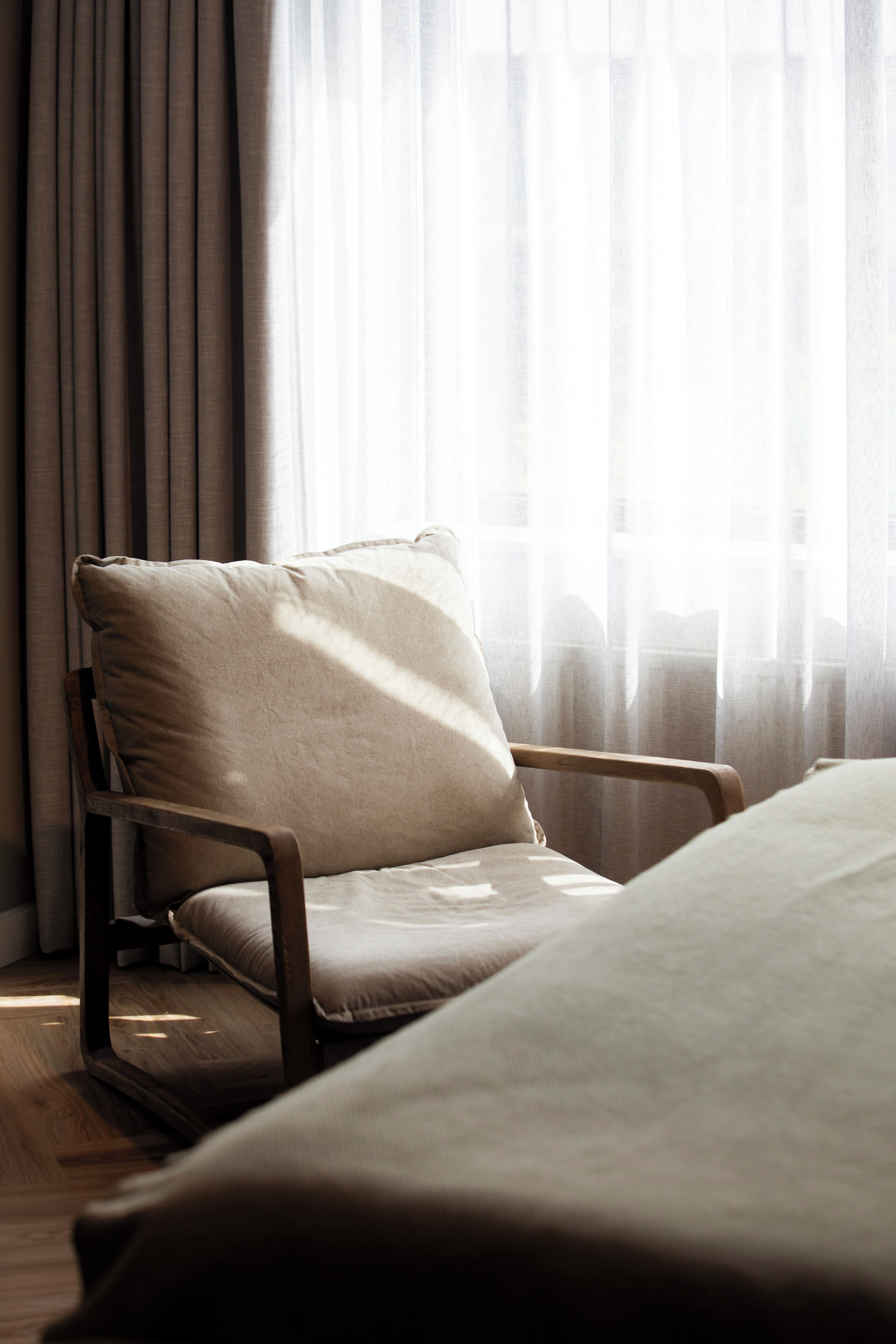 Ein Zimmer mit Holzstuhl und Bett, einem fenster mit Vorhängen und Holzboden.