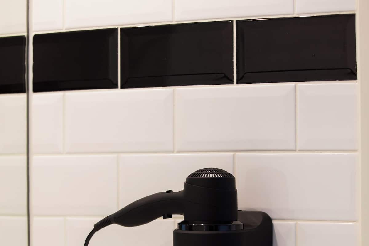 Un secador de pelo negro fijado a una pared de azulejos blancos.