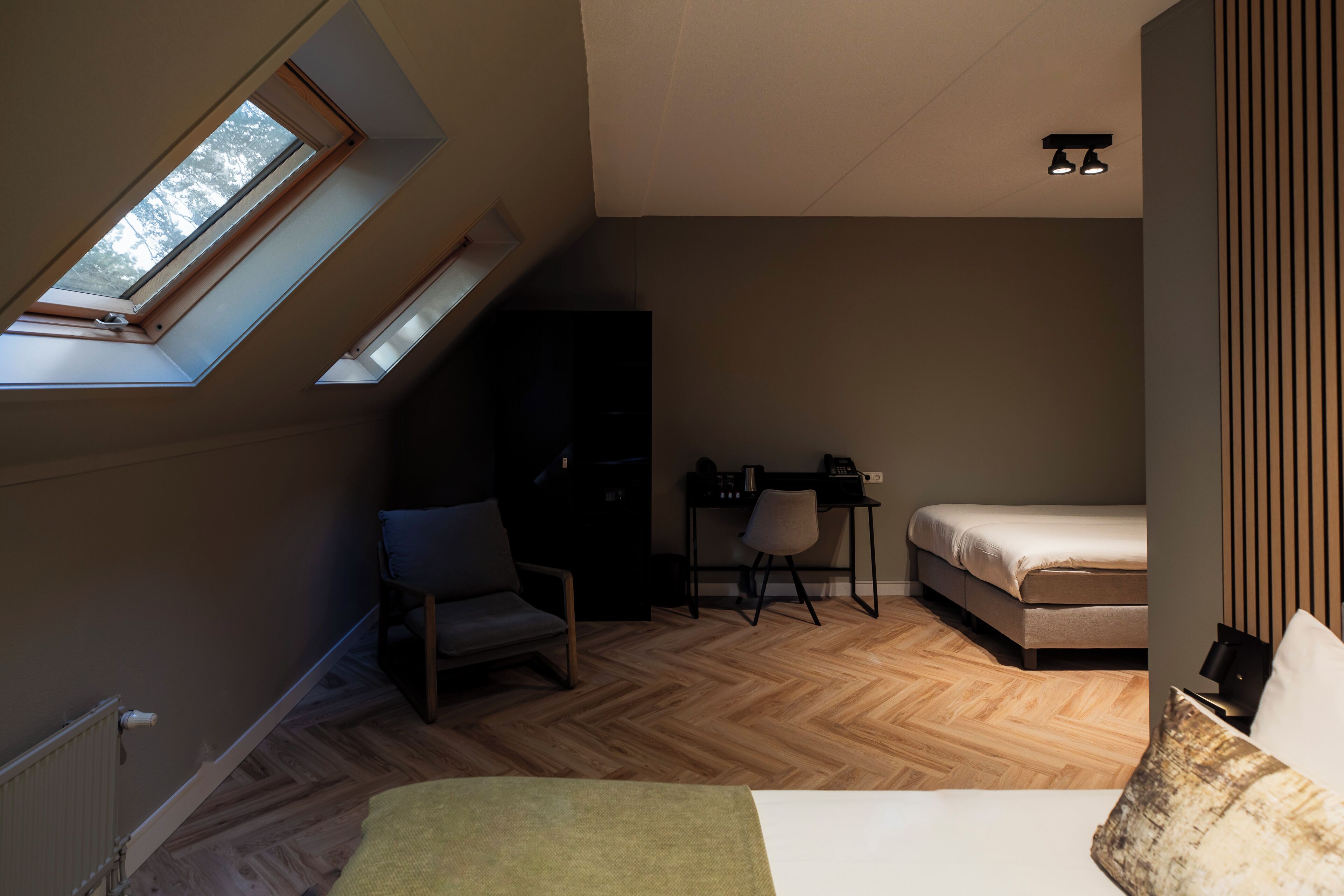 Ein Schlafzimmer mit Schrägdecke, Dachfenster, einem Bett, einem Schreibtisch, einem Stuhl und einer Heizung.