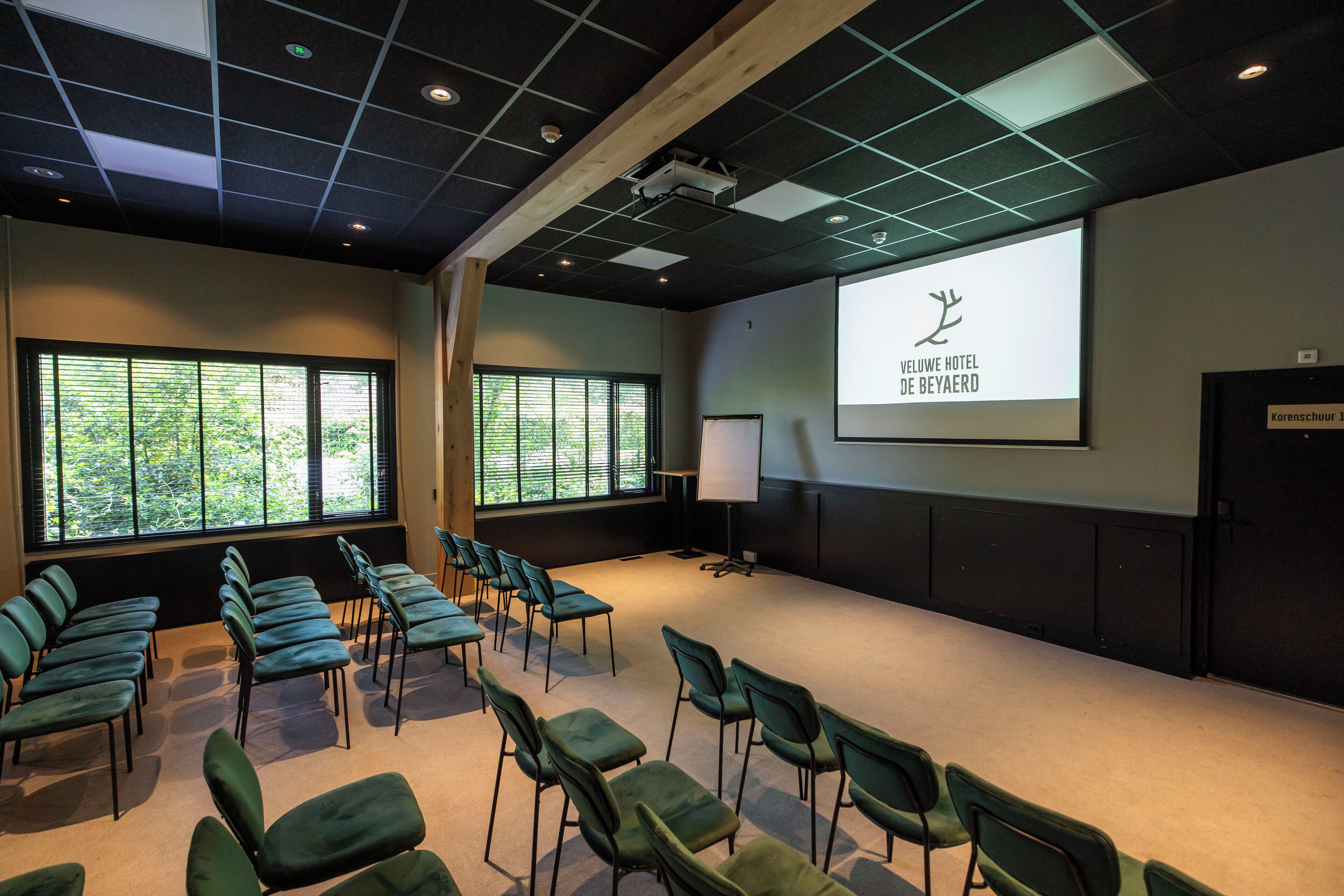 A conference room with rows of chairs, a projector screen, and a large window with blinds.