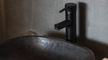 Un baño moderno con un lavabo de piedra grande y redondo, un grifo negro y un dispensador de jabón negro fijado a la pared.