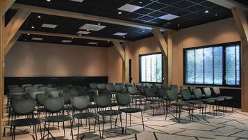 Un salón de conferencias con filas de sillas, una pantalla para proyector y un amplio ventanal con persianas.