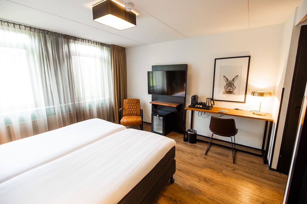 Habitación de hotel con una cama grande, un escritorio con una computadora, un televisor y un cuadro en la pared.