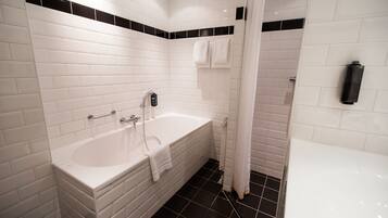 Un baño moderno con azulejos blancos tipo metro, una bañera blanca, zona de ducha y suelo negro.