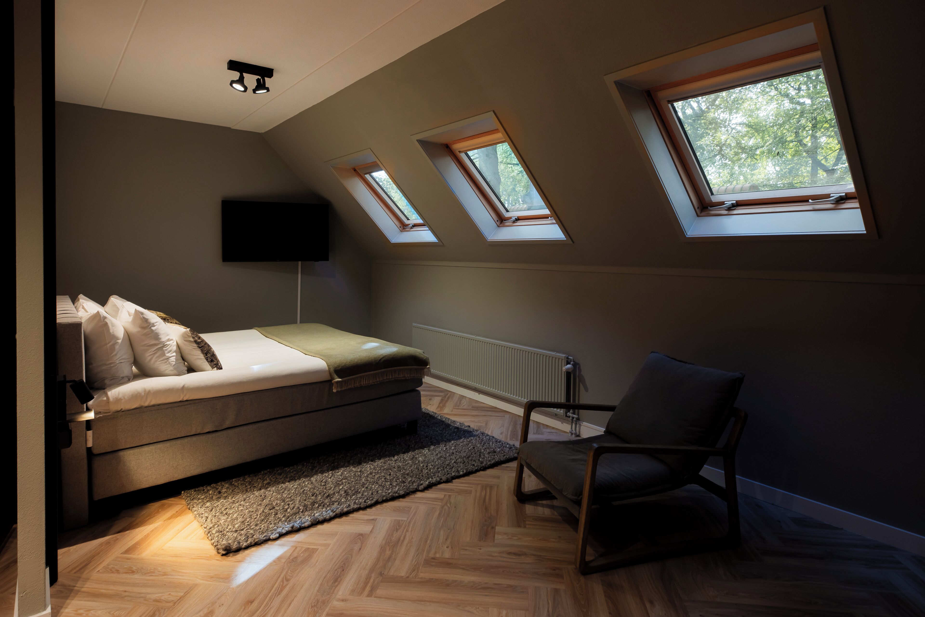 Un dormitorio con cama, una silla, televisor y tragaluces.