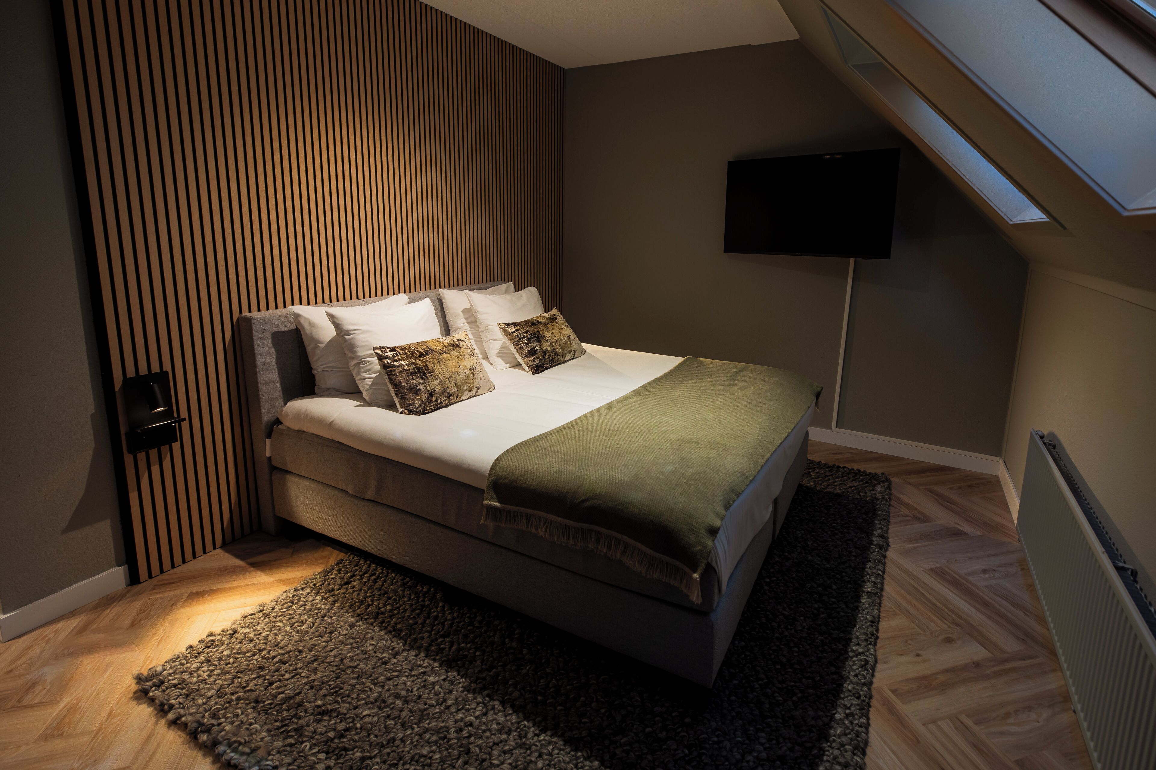 A modern bedroom with a bed, a TV mounted on the wall, and a wooden slat wall design.